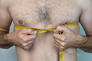 Caucasian thin man with chest hair measuring it with tape measure